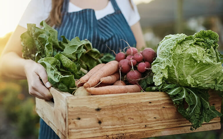 Femme portant une cagette de légumes